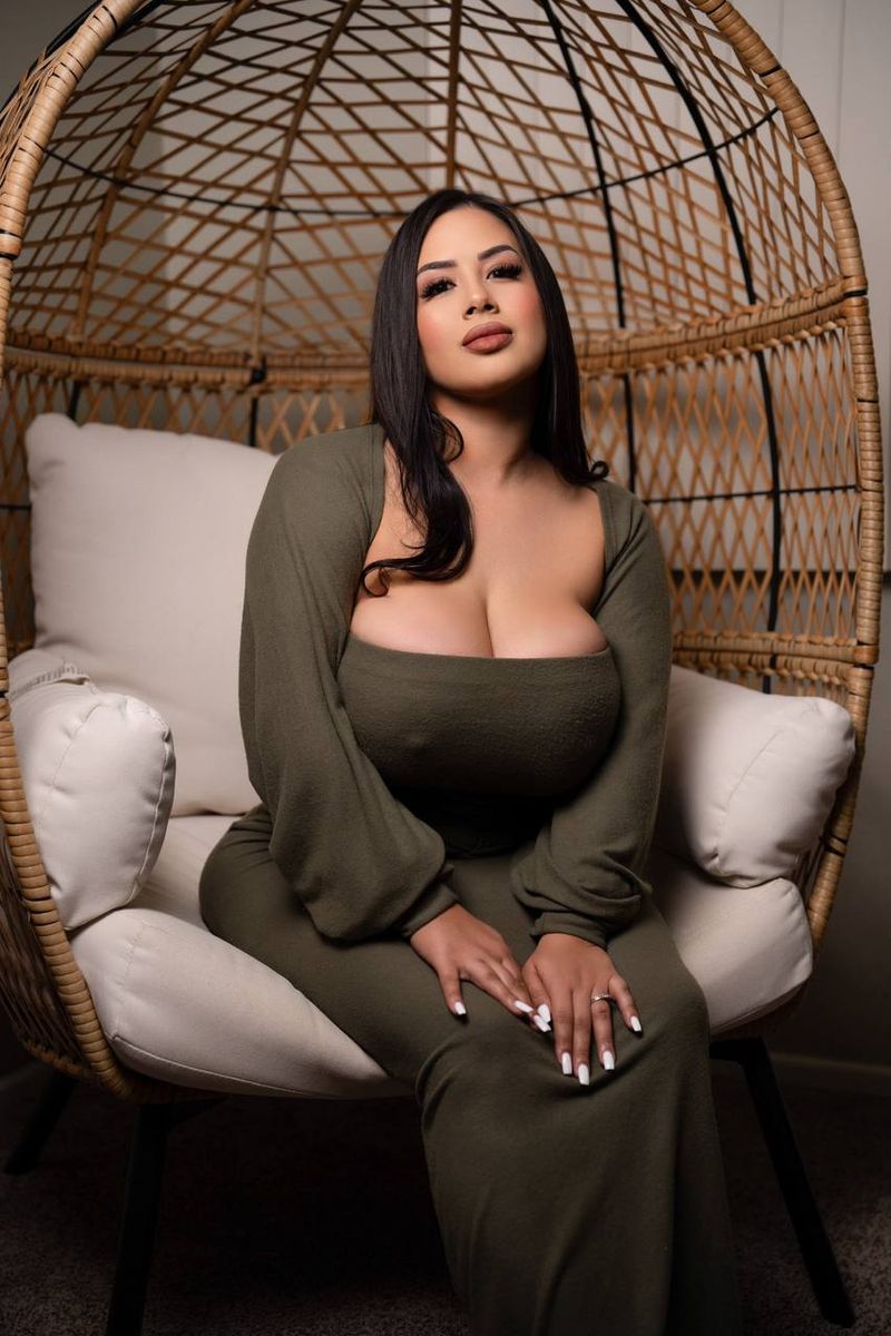 Alivia seated in a woven rattan egg chair, wearing an olive green long-sleeve dress